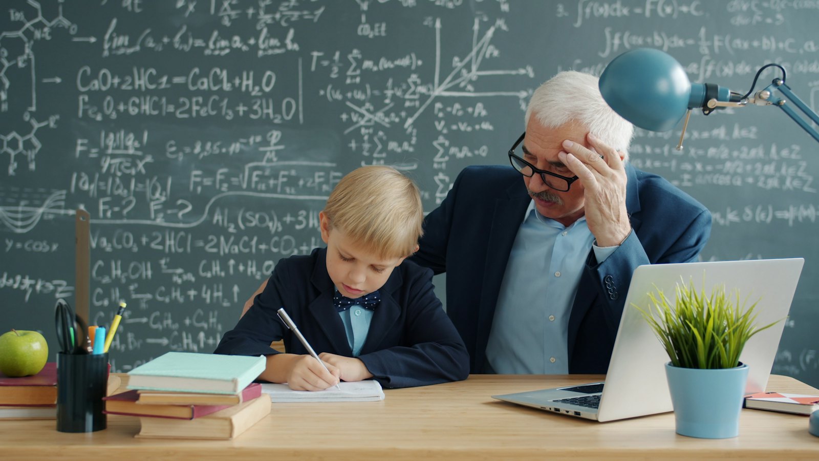 Lektor s chlapcem u stolu před tabulí se vzorci